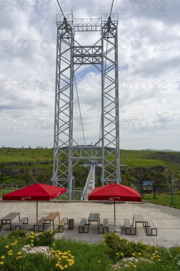 A tall metal structure with seating and red umbrellas in the foreground of nature, Diamond Bridge, Diamond Glass Bridge, world's longest free-hanging structure, Dashbashi Gorge, Khrami River, Chram, Tsalka Nature Reserve, Kartli, Georgia