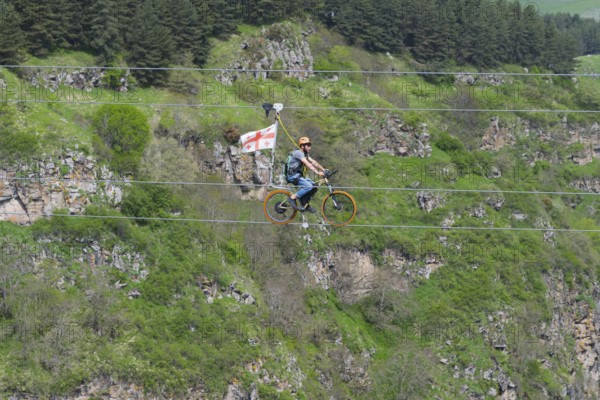 Person riding a bicycle on a rope in front of a wooded rocky landscape in the mountains, Dashbashi Gorge, Khrami River, Tsalka Nature Reserve, Kartli, Georgia
