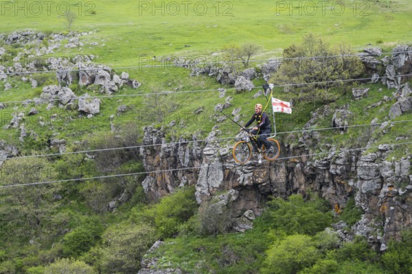 Person riding a bicycle on a stretched rope across a gorge in green countryside, Dashbashi Gorge, Khrami River, Tsalka Nature Reserve, Kartli, Georgia