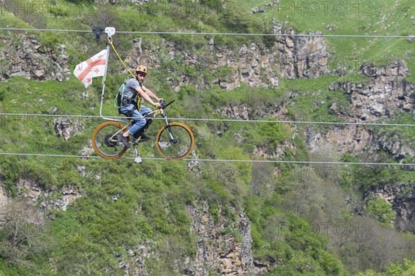 Man on a bicycle balancing at lofty heights above a green valley, Dashbashi Gorge, Khrami River, Tsalka Nature Reserve, Kartli, Georgia