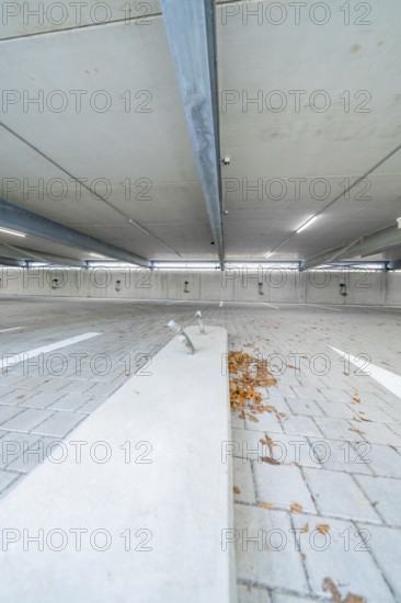 Empty parking lot with concrete floor, scattered leaves and parking space markings, parking garage construction with charging infrastructure, Calw, Germany