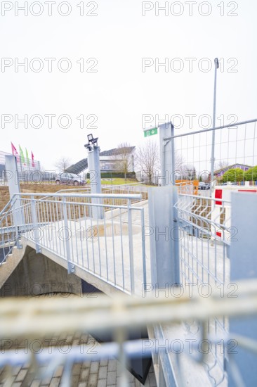 Modern outdoor area with steel railings and flags, building complex in the background, parking garage construction with charging infrastructure, Calw, Germany