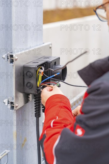Person wearing a red jacket assembles electrical cables at a metal station, parking garage construction with charging infrastructure, Calw, Germany