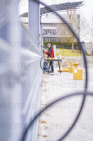 A man cleans a railing in front of a modern building complex in winter, parking garage construction with charging infrastructure, Calw, Germany