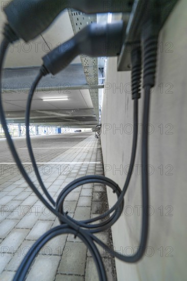 Charging cables hang on a concrete wall under ceiling in a parking garage, parking garage construction with charging infrastructure, Calw, Germany