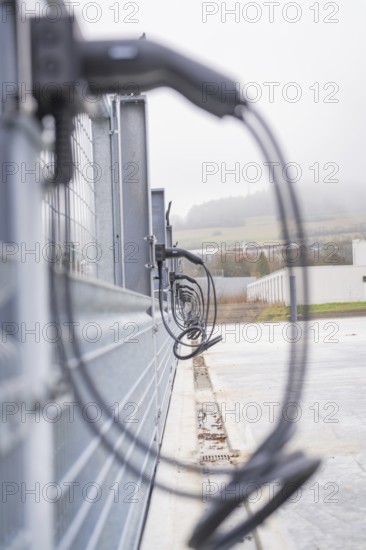 Cables run along a fence in an industrial environment, with foggy weather, parking garage construction with charging infrastructure, Calw, Germany