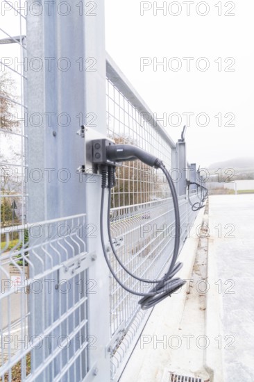Cables are attached to a metal fence, with cloudy weather in the background, parking garage construction with charging infrastructure, Calw, Germany