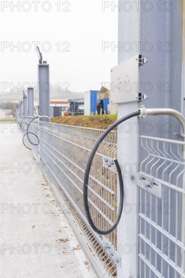 Electrical cable in front of a grey fence in an industrial area, parking garage construction with charging infrastructure, Calw, Germany