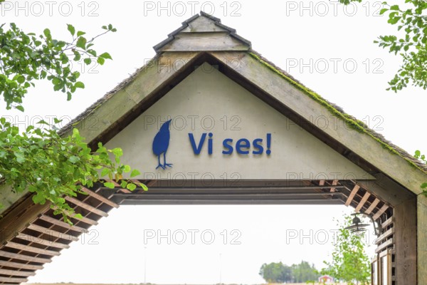 Welcome sign under a rustic wooden roof with green leaves, Vogelsee Tåkern, Vadstena, Östergötalands Län, Sweden