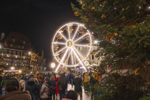 Illuminated Ferris wheel and half-timbered houses at night on a busy Christmas market, Weihnachtsmark Nagold, LandkreisCalw, Germany