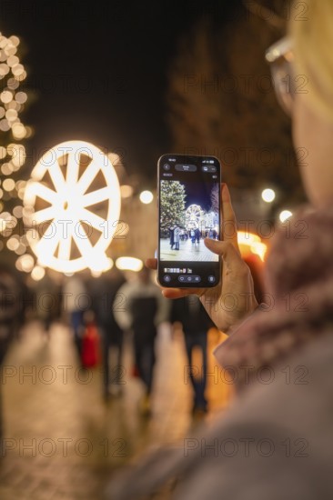 A person photographs a glowing Ferris wheel at a Christmas market, Weihnachtsmark Nagold, LandkreisCalw, Germany