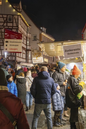 Night market visitors at an illuminated cotton candy stand in front of half-timbered houses, Weihnachtsmark Nagold, LandkreiScalw, Germany