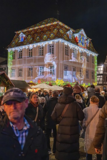 People in a festive square at night with an artistic light show on a building, Weihnachtsmark Nagold, LandkreisCalw, Germany