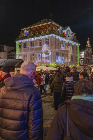 People at a Christmas market in front of an illuminated historic building with a projection, Weihnachtsmark Nagold, LandkreisCalw, Germany