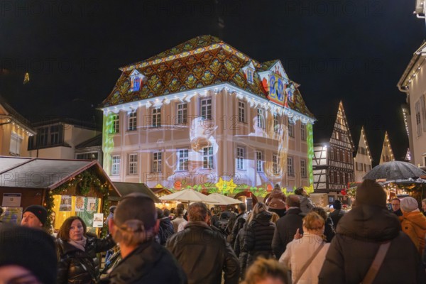 Lively scene at a market with light projection onto a building and people celebrating, Weihnachtsmark Nagold, LandkreisCalw, Germany