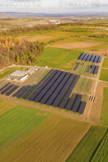 Solar systems in fields surrounded by autumn trees and a village, Energiewende, construction of PV open space, Baden-Württemberg, Germany