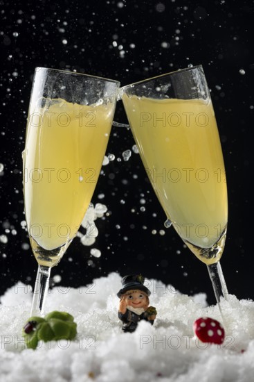 Two sparkling champagne glasses in the snow with lucky New Year's Day charms