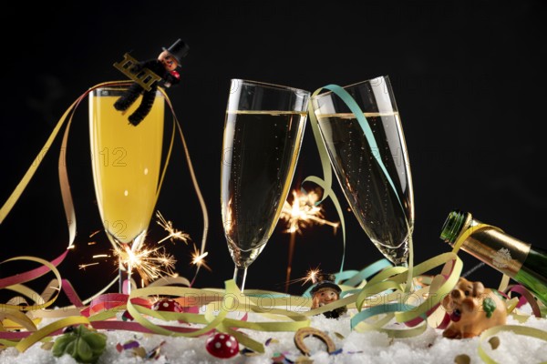 Three champagne glasses with lucky New Year's Day charms, streamers and sparklers in the snow