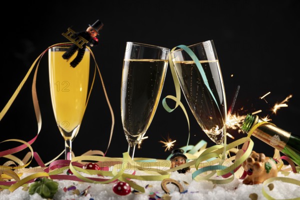 Three champagne glasses with lucky charms for New Year, streamers and sparkler in the snow