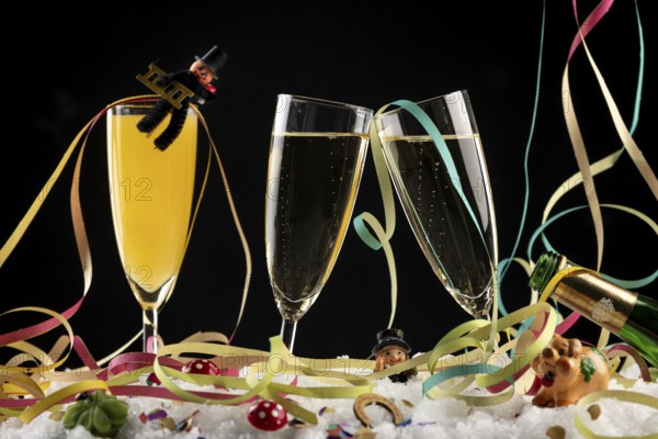Three champagne glasses with lucky charms for the New Year and streamers in the snow