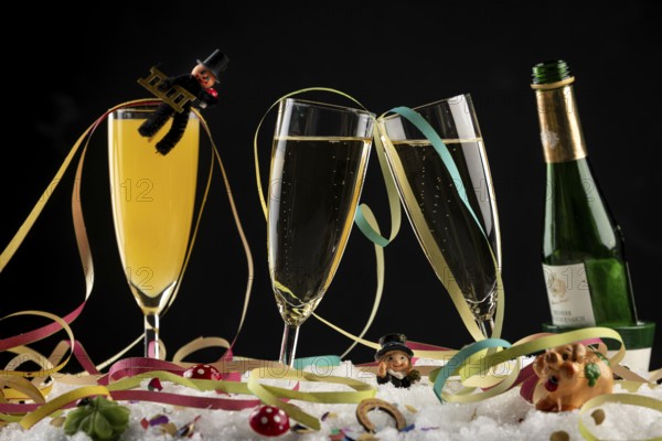 Champagne bottle, glasses with sparkling wine, streamers and lucky charms in the snow