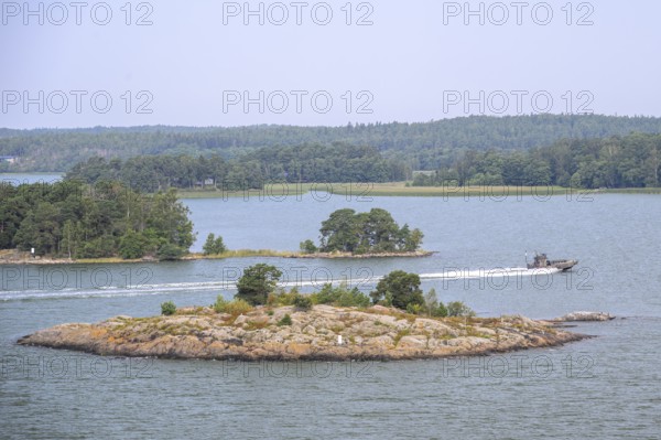 Small, wooded island in calm water with passing patrol boat boat, marine speedboat, Aaland Islands, Finland