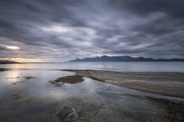 The Vestfjord in Nordland, Norway, near Bodø, impresses with a dramatic atmosphere. Dark clouds sweep across the water and create a mystical atmosphere. The rugged cliffs and majestic mountains are reflected in the tranquil fjord and provide an impressive backdrop