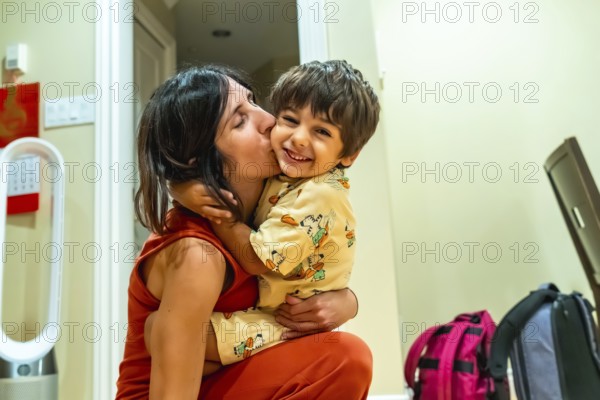 Happy mother kissing her cheerful son on the cheek while holding him in her arms, enjoying a warm moment together in their cozy home in vancouver, british columbia