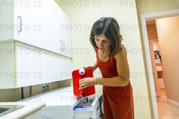 Housewife carefully pouring blue laundry detergent from a red container into the washing machine drawer in a modern laundry room in vancouver