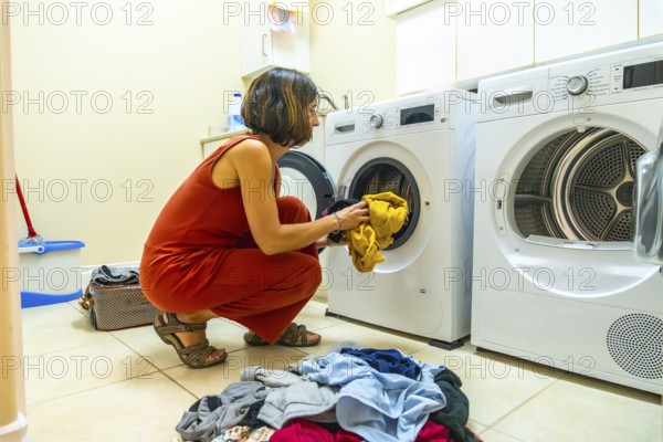 Woman loading clothes into a washing machine in a bright, modern laundry room, engaging in regular household chores and maintaining a tidy, organized home environment