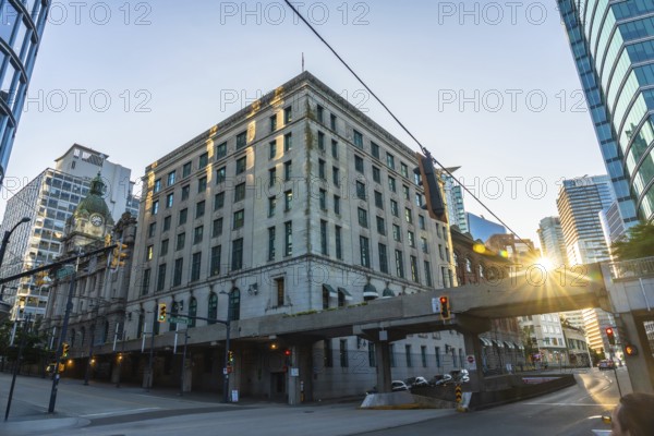 Sun is rising behind waterfront station, casting warm glow on historic building and modern skyscrapers in vibrant downtown vancouver, british columbia
