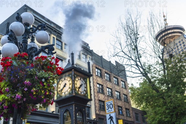 Gastown steam clock releasing clouds of steam amidst vibrant flowers, with the iconic harbour centre rising in the background, creating a picturesque scene in vancouver, british columbia