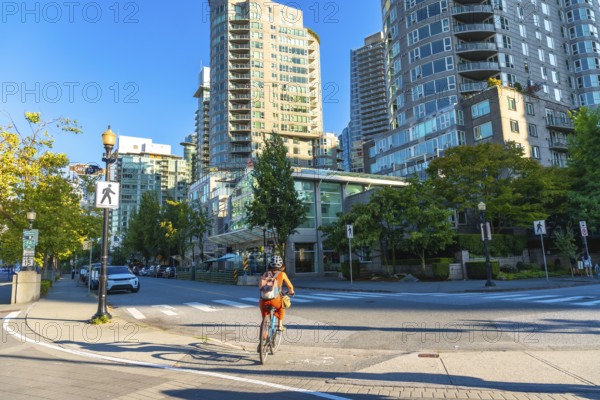 Cyclist enjoying a sunny day, riding a bicycle on a dedicated bike lane in the city center of vancouver, surrounded by modern residential buildings and green trees