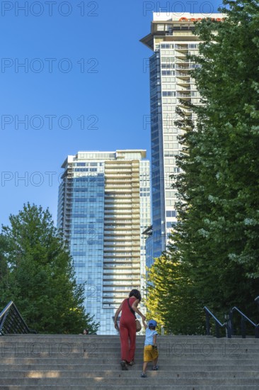 Mother and son climbing stairs together, surrounded by towering skyscrapers and lush trees in downtown vancouver, british columbia, enjoying a sunny summer day in the vibrant city