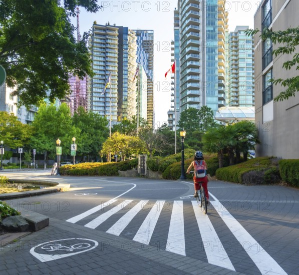 Canadian flag waving between modern buildings while a woman with backpack and helmet rides her bicycle in vancouver downtown, british columbia