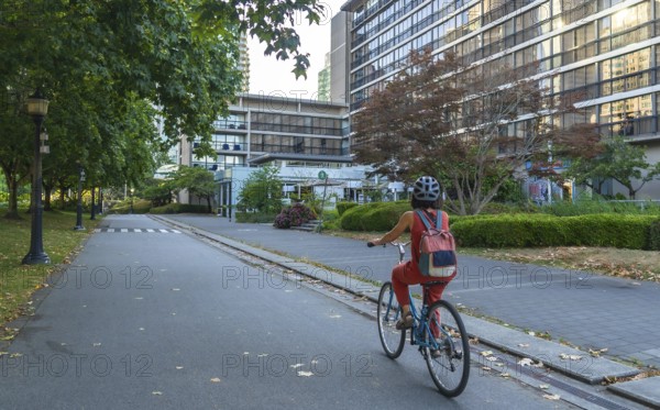 Woman with backpack and helmet is riding a bicycle on a dedicated bike lane next to a park, enjoying her urban commute in vancouver, british columbia