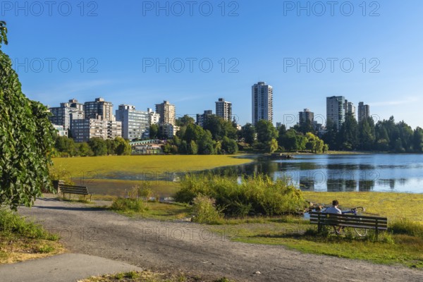 Vancouver city skyline reflecting on trout lake with yellow algae bloom during summer in british columbia, canada, a cyclist is relaxing on a bench enjoying the view
