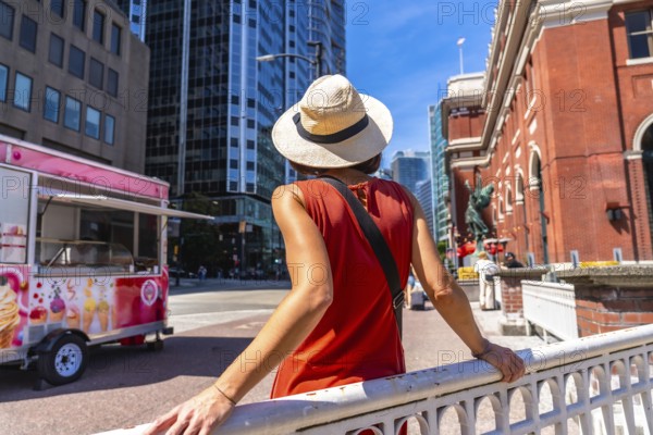 Young woman wearing a straw hat and an orange dress is enjoying the urban landscape of vancouver. British columbia. With a food truck and a historic building in the background on a bright summer day