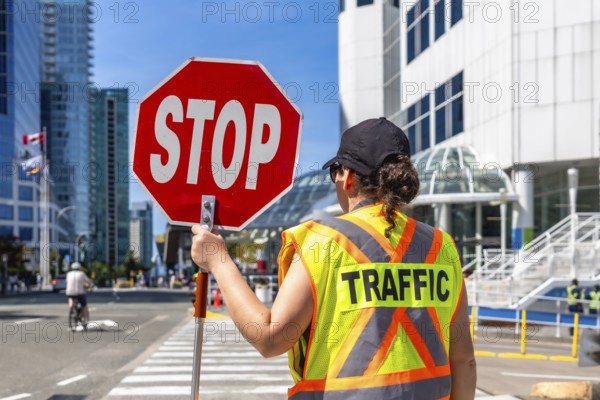 Traffic guard wearing high visibility vest holding stop sign regulating traffic flow on a city street in vancouver. British columbia. Canada. Ensuring pedestrian safety and efficient vehicle movement