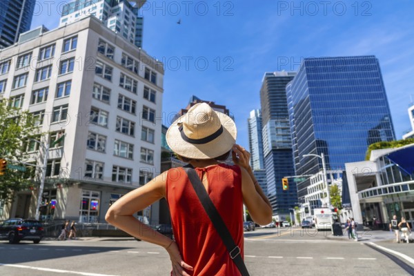 Young woman wearing a straw hat enjoying the cityscape of vancouver, british columbia, on a vibrant summer day, taking in the modern architecture and bustling urban atmosphere
