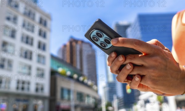 Close up of hands holding smartphone with multiple camera lenses, using navigation app in vancouver city center, with blurred buildings in background on sunny day