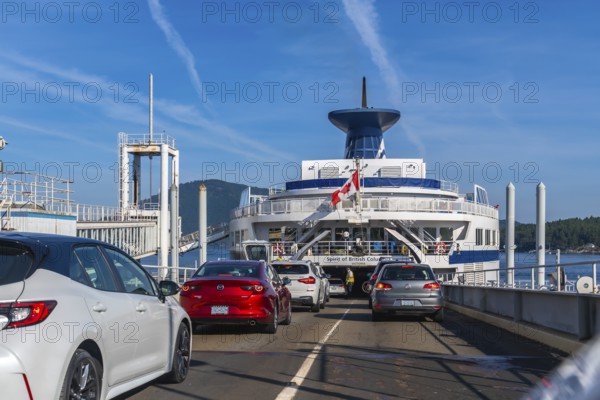 Cars are boarding a ferry with a canadian flag, departing from victoria on vancouver island to vancouver, british columbia, on a sunny day with blue skies