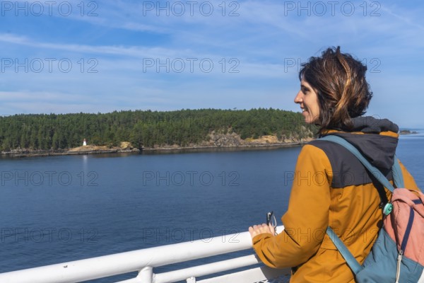 Tourist leaning on the ferry railing, enjoying breathtaking ocean views and a small island with a lighthouse during a scenic journey from victoria to vancouver