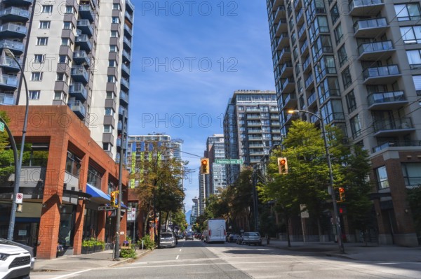 Modern residential and commercial buildings line a busy street in vancouver, british columbia, with cars and a delivery truck navigating the urban landscape under a clear blue sky