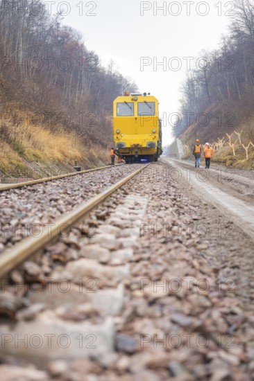 Yellow work train runs on a railroad track with workers on the line, stuffing machine on Hermann, Hesse, Bahn, Althengstett, Calw district, Germany