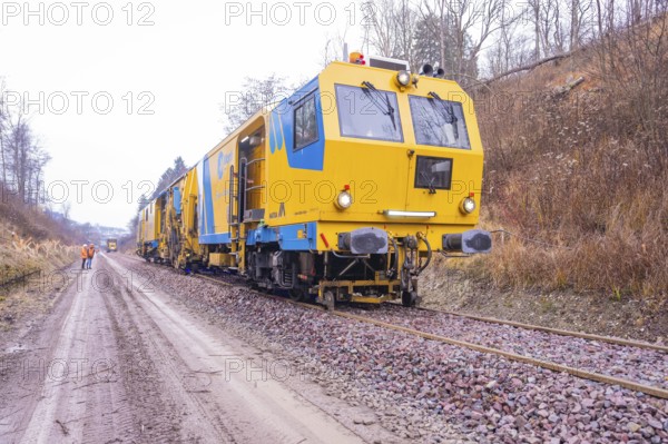 Yellow working trains on railroad tracks in a wintry landscape with gravel, stuffing machine on Hermann, Hesse, railway, Althengstett, Calw district, Germany