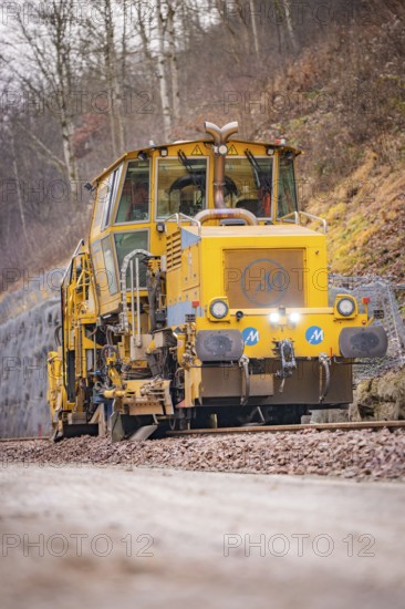 Yellow track construction machine runs on railroad tracks through wooded area, stuffing machine on Hermann, Hesse, Bahn, Althengstett, Calw district, Germany