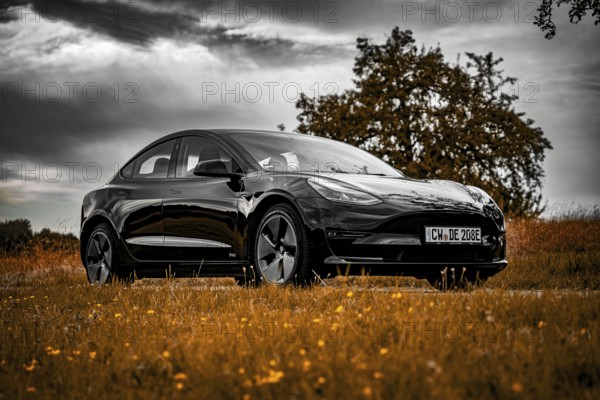 Black car parked on country road, dramatic clouds in the sky surrounded by meadows, Deer E-Carsharing, Tesla Model 3, Calw, Germany