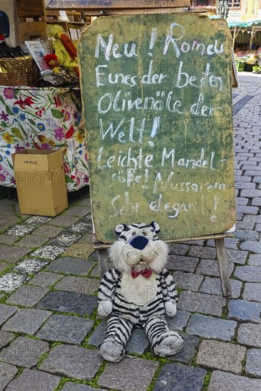 Blackboard, chalk script, funny advertisement, letters, market scene, stuffed tiger, plush toy with fly, paving stones, best olive oil, Tübingen, Baden-Württemberg, Germany