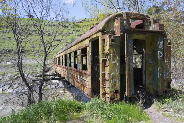 An abandoned, rusted drawbridge with graffiti in a green, hilly landscape on the riverbank, discarded railroad car used as a footbridge, Paravani river, Akhalkalaki, Akhalkalaki, Samtske-Javakheti region, Samtske Javacheti, Lesser Caucasus, Georgia
